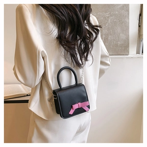 Detail of black matte leather mini crossbody bag with a 3D pink bow and silver chain strap