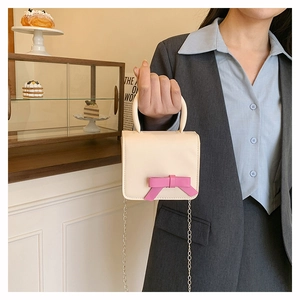 Mini cream PU leather bag with pink bow detail and metal chain strap held by model
