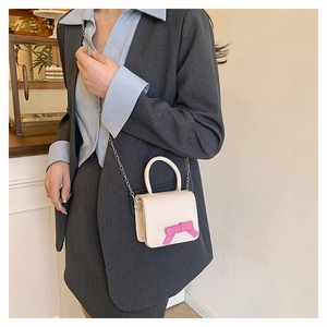 Detail of a mini cream crossbody bag with a pink bow and silver chain strap
