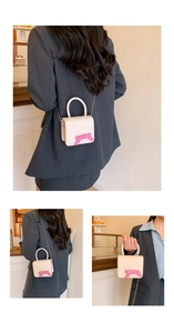 Mini cream crossbody bag with pink bow accent and metal chain strap shown on model