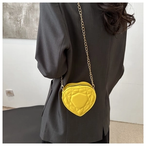Detail of yellow heart-shaped crossbody bag featuring classic quilted pattern and gold chain