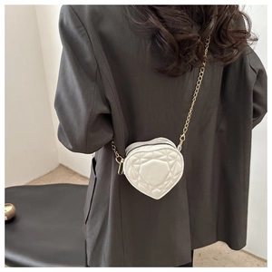 Back view of a model wearing a white heart-shaped quilted crossbody bag with gold chain strap