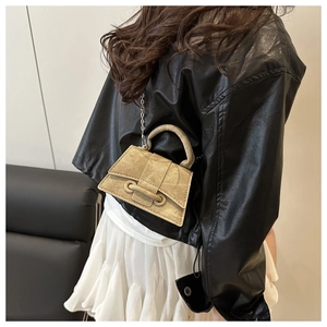 Detail of a champagne gold leather mini crossbody bag with silver chain strap worn by a model