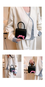 Close-up of black mini crossbody bag featuring a pink bow and silver metal chain strap
