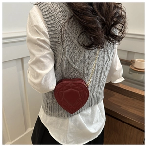 Model wearing red heart-shaped crossbody bag with gold chain strap and quilted pattern