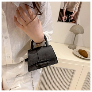 Detail of a minimalist black mini bag with silver chain strap held by a model
