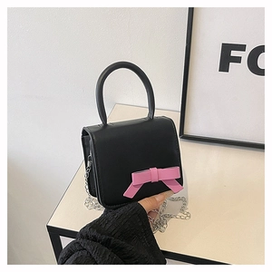 Detail of a black crossbody bag with a large pink bow and silver chain strap