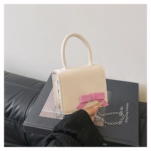 Close-up of cream mini crossbody bag with a pink bow and elegant metal chain strap