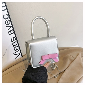 Detail of silver bow crossbody bag featuring a pink ribbon and metallic chain strap