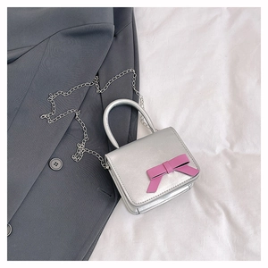 Detailed close-up of a silver mini bag featuring a pink bow on a grey blazer backdrop