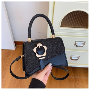 Détail d'un sac bandoulière noir avec boucle fleur dorée et paillettes scintillantes
