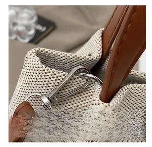 Detail of silver metal hook and brown leather handle on off-white woven canvas tote bag