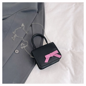 Detail of black mini crossbody bag with a pink bow and silver chain on a grey blazer