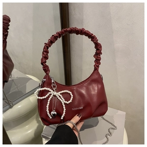 Detail of burgundy soft leather bag featuring pleated handle and pearl bow charm