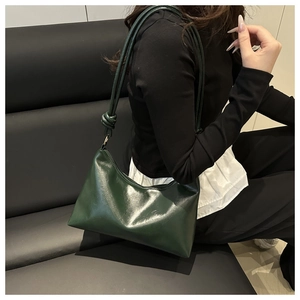 Détail d'un sac cabas en cuir verni vert foncé avec un nœud décoratif sur la bandoulière