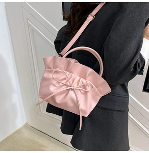 Détail du sac bandoulière rose plissé avec nœuds porté sur un blazer noir oversize