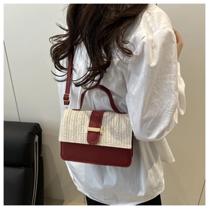 Detail shot of a red leather and woven straw crossbody bag shown on a female model
