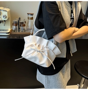 Détail du sac à main blanc à volants avec nœud, porté par un mannequin dans un café