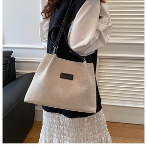 Side view of model wearing a large beige canvas tote bag with black leather straps