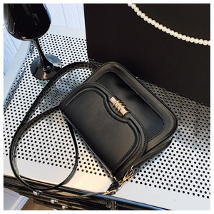 Detail of a black leather crossbody bag featuring a golden circular metal clasp lock