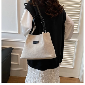 Detail shot of beige canvas tote bag with black leather label and fashion logo