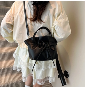 Detail of black pleated bucket bag with bow tie on model wearing white lace dress