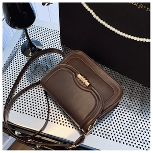 Detail of vintage brown leather crossbody bag featuring a curved flap and gold metal lock