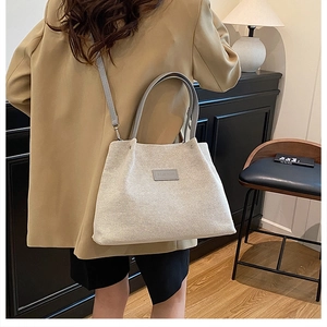 Detail of a minimalist cream canvas tote bag featuring grey straps and Fashion leather patch
