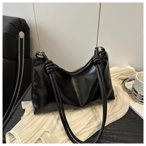 Détail du sac hobo noir brillant avec bandoulières à nœuds sur un tissu plissé blanc