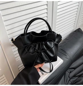 Detail view of a black pleated cloud bag with a decorative bow and metallic D-rings
