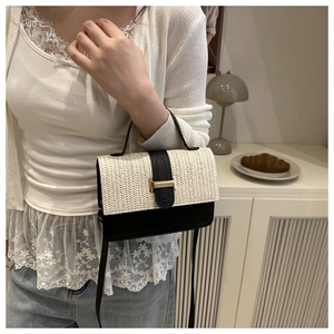 Detail view of woven straw flap and black leather handle with golden metal buckle clasp
