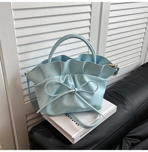Détail du sac à main bleu clair avec bords ondulés et nœud papillon sur fond de livre