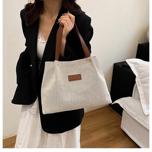 Close-up of cream canvas tote bag with brown leather handles and FASHION logo patch