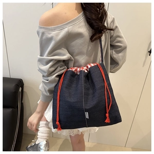 Detail of denim crossbody bag featuring orange drawstring closure and red gingham lining