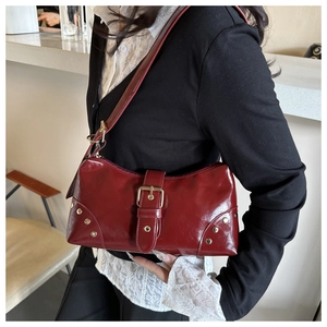 Close-up of wine red glossy leather tote featuring a gold buckle and metallic rivets