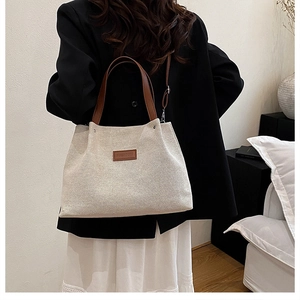Detail of minimalist canvas tote bag featuring brown leather handles and FASHION patch