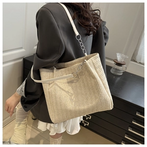 Detail of a beige woven tote bag with white leather straps and metallic chain accents