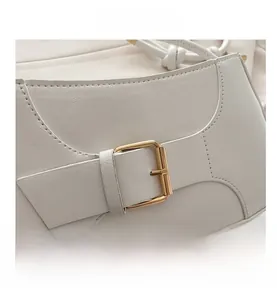 Detail of white lychee leather texture and gold metal buckle on a stylish shoulder bag