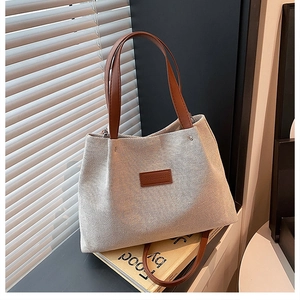 Detail of woven canvas tote bag with brown leather handles and fashion logo on stone surface