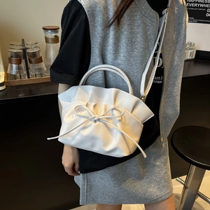 Sac nuage blanc en cuir plissé avec nœud porté par un mannequin dans un café moderne