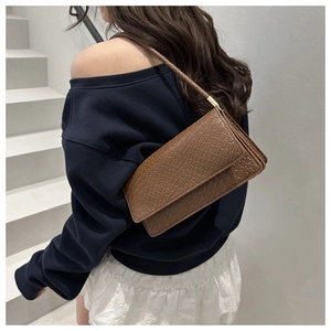 Detail shot of brown baguette bag featuring a textured woven pattern and gold hardware