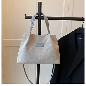 Detail of grey-blue woven tote bag featuring a leather patch with embossed text and handle