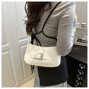 Detail of white leather shoulder bag featuring a large golden buckle and wide strap accent