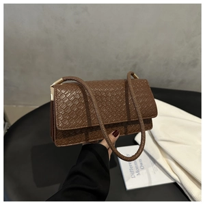 Detail of brown crocodile pattern small shoulder bag with woven strap and metal handle