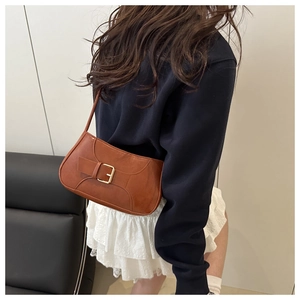 Brown leather underarm bag with gold buckle shown on shoulder for classic styling
