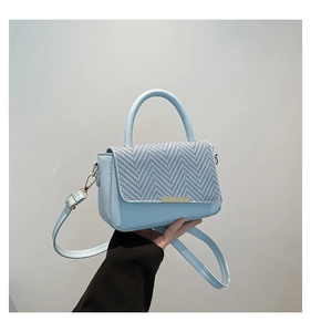 Close-up of light blue handbag featuring a chevron weave pattern and gold metallic clasp