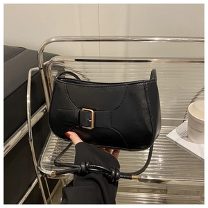 Detail of black glossy leather shoulder bag with gold metal buckle and knotted strap