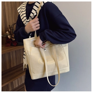 Detail view of the large beige canvas tote bag showing the front pocket and print