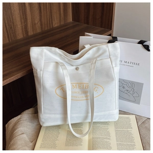 Detail of white canvas tote bag with yellow logo pocket in a cozy lifestyle setting