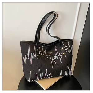 Détail de la broderie ondulée colorée et de l'étiquette en cuir sur le sac cabas noir